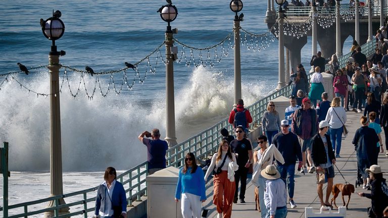 Visitors to Manhattan Beach pier watch as turbulent surf pounds the side of the pier in Manhattan Beach, Calif. on Thursday, Dec. 28, 2023. (AP Photo/Richard Vogel)