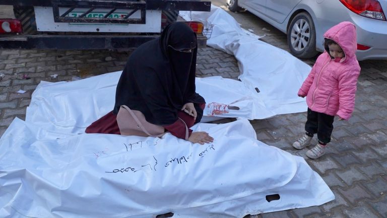 Woman in Gaza strokes a covered body while a little girl watches 