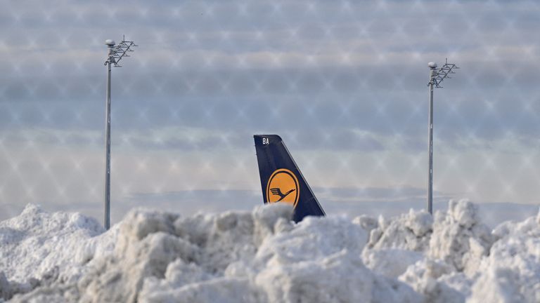 A tail fin of a Lufthansa plane is pictures behind snow at the terminal as Munich Airport has cancelled all incoming and outgoing flights until 12 p.m. (1100GMT) due to a forecast for sleet in Munich, Germany, December 5, 2023. Picture taken through a fence. REUTERS/Angelika Warmuth
