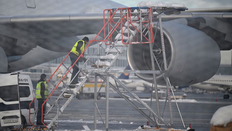 Workers clear a towable passenger staircase from snow as Munich Airport has cancelled all incoming and outgoing flights until 12 p.m. (1100GMT) due to a forecast for sleet in Munich, Germany, December 5, 2023. Picture taken through a fence. REUTERS/Angelika Warmuth
