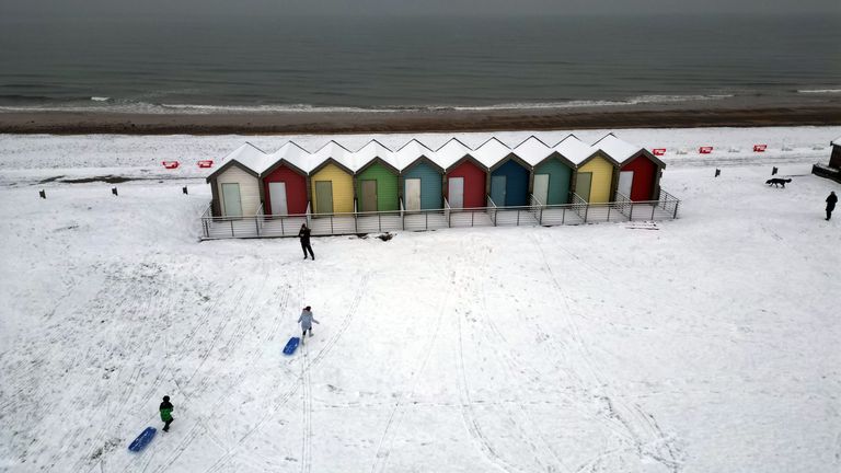 People walk through the snow beside the beach huts at Blyth in Northumberland, as temperatures are tipped to plunge to as low as minus 11C in parts of the UK over the weekend. Picture date: Sunday December 3, 2023.