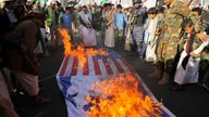 People gather near burning Israeli and US flags, as supporters of the Houthi movement rally to denounce air strikes launched by the US and Britain