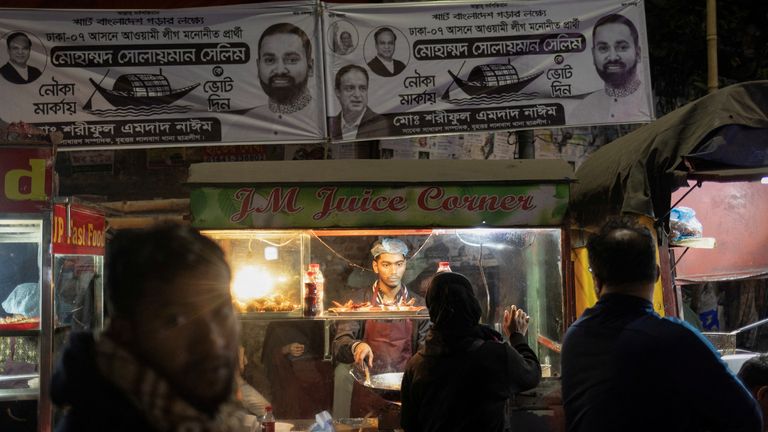 People buy snacks from a road side vendor as election campaign posters of Awami League are hung over a street, ahead of the general election, in Dhaka, Bangladesh, January 5, 2024. REUTERS/Adnan Abidi