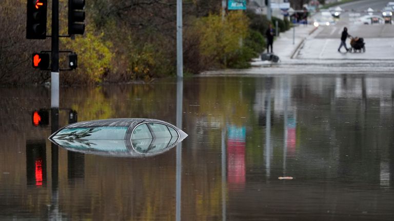 A car sits partially submerged on a flooded road during a rain storm  
Pic: AP