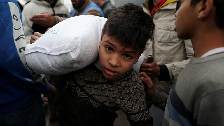 A Palestinian boy carries a bag of flour distributed by UNRWA