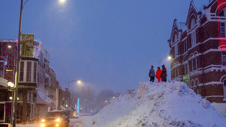 People stand on an enormous snow pile in downtown Oskaloosa, Iowa, on Tuesday. Pic:AP