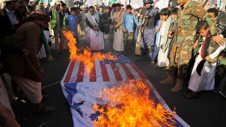 People gather near burning Israeli and US flags, as supporters of the Houthi movement rally to denounce air strikes launched by the US and Britain