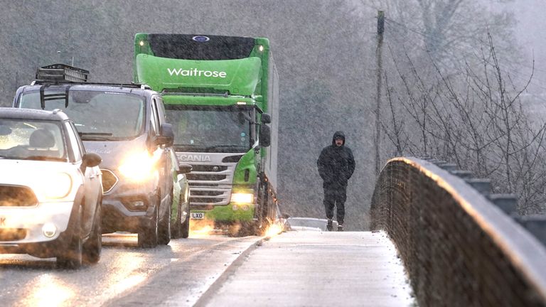A pedestrian passes queuing vehicles on a motorway bridge as he walks through a snow shower near Maidstone in Kent. Sleet and snow showers have been forecast for parts of the country on Monday as some regions are still trying to grapple with flooding following intense rainfall. Picture date: Monday January 8, 2024. PA Photo. See PA story WEATHER Rain. Photo credit should read: Gareth Fuller/PA Wire.