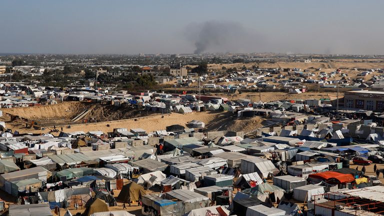 A tent camp housing displaced Palestinians, as smoke rises in the distance due to an Israeli ground operation in Khan Younis