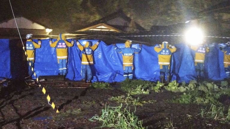 Police use blue sheets as a woman in her 90s is rescued alive from a collapsed house in Suzu. Pic: AP