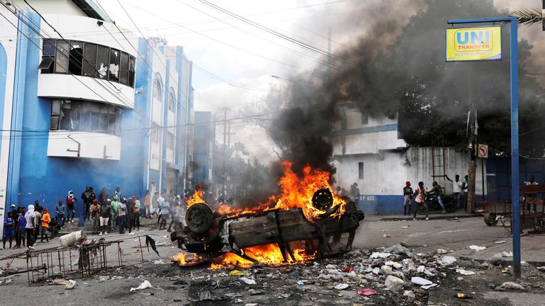 People stand near a burning car.
Pic: Reuters