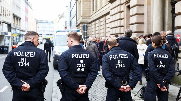 Police officers stand guard as people queue at the entrance of the court where  Christian B is due to appear.
Pic: Reuters