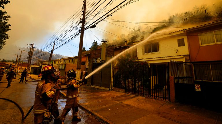 Firefighters protectively spray water on homes as forest fires burn nearby, in Vina del Mar, Chile, Saturday, Feb. 3, 2024. Officials say intense forest fires burning around a densely populated area of central Chile have left several people dead and destroyed hundreds of homes. (AP Photo/Esteban Felix)