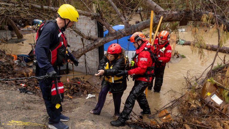 Firefighters rescue a woman from a homeless encampment that became surrounded by floodwater in the Santa Ana River during a rainstorm, Monday, Feb. 5, 2024, in San Bernardino, Calif. (AP Photo/Ethan Swope)