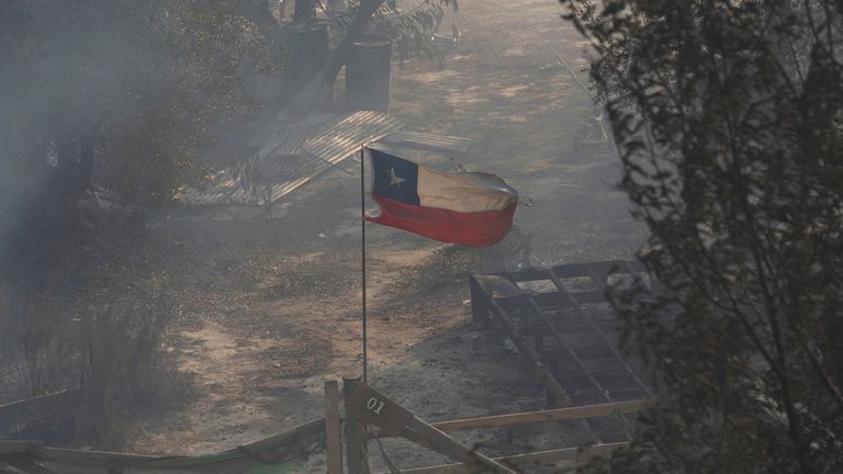 Chile&#39;s national flag flies amidst smoke and near the burnt remains of a house following the spread of wildfires, in Vina del Mar, Chile February 3, 2024. REUTERS/Sofia Yanjari
