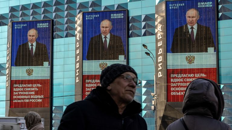 People wait for a bus under an image of Vladimir Putin and a quote from his annual address. Pic: Reuters