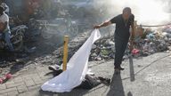 A person lifts a sheet to look at a body in the Petion-Ville neighborhood. Pic: AP