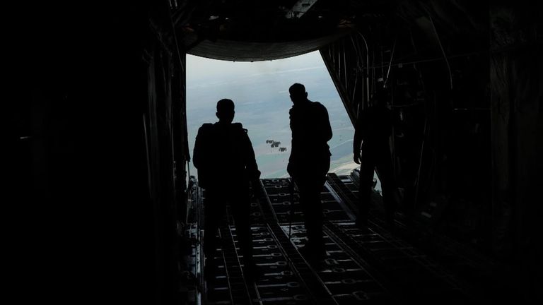 Jordan air force members watch as crates of aid fall toward Gaza. 