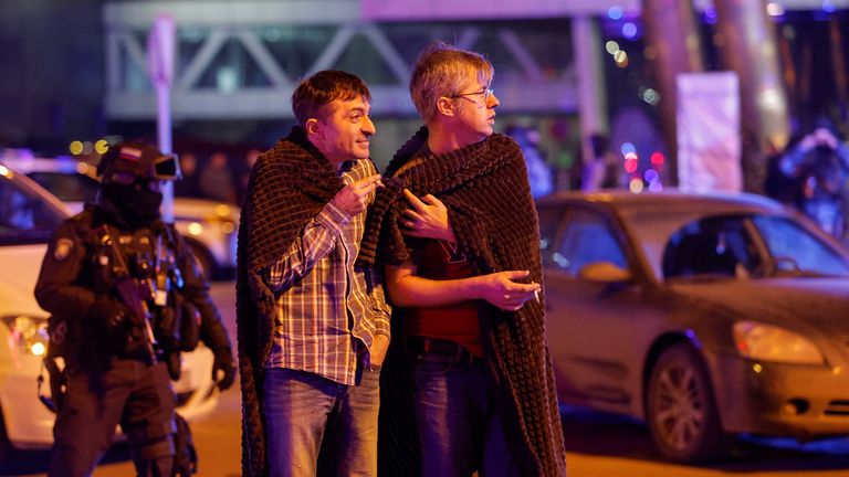 Men cover themselves with blankets near the burning Crocus City Hall. Pic: Reuters