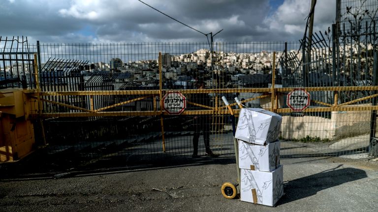 An IDF soldier stands guard behind an Israeli checkpoint for Hebron, with boxes of aid outside.