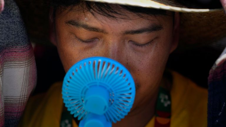 FILE - A World Youth Day volunteer uses a small fan to cool off from the intense heat, as he waits ahead of the Pope Francis arrival at Passeio Mar..timo in Alg..s, just outside Lisbon, Aug. 6, 2023. The European climate agency calculates that November, for the sixth month in a row, the globe set a new monthly record for heat, adding the hottest autumn to the broken records of record-breaking heat this year. (AP Photo/Armando Franca, File)