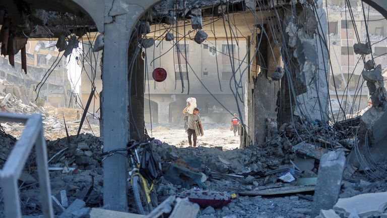 一名巴勒斯坦男子在以色列袭击汗尤尼斯后，在一栋被毁坏的住宅楼的废墟中行走时携带财物。