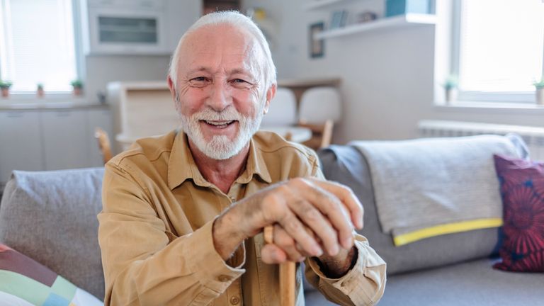 Shot of a happy elderly man sitting on the couch with a walking stick at home. Pic: iStock.