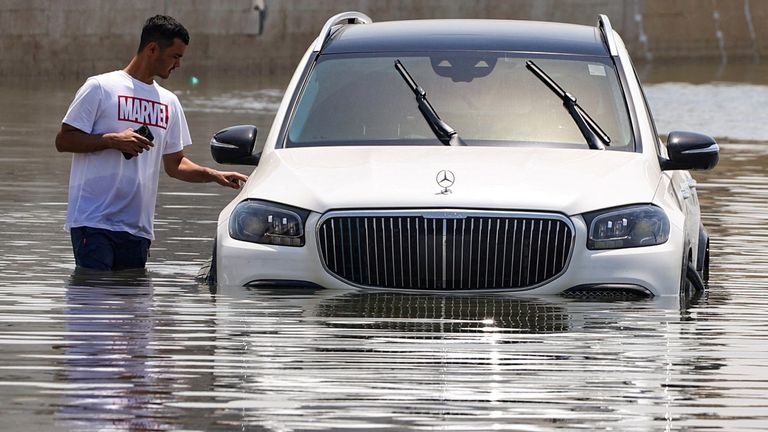 مردی در کنار خودرویی ایستاده است که در اثر سیل پس از باران شدید در دبی تا حدی زیر آب رفته است.  عکس: رویترز