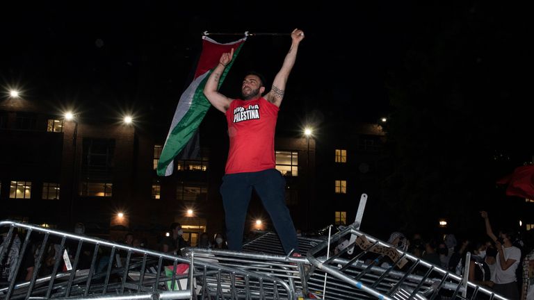 A George Washington University student waves a Palestinian flag as he stands atop police barricades that students broke through to occupy the school's University Yard during a pro-Palestinian protest in Washington, Sunday, April 28, 2024. (AP Photo/Cliff Owen)