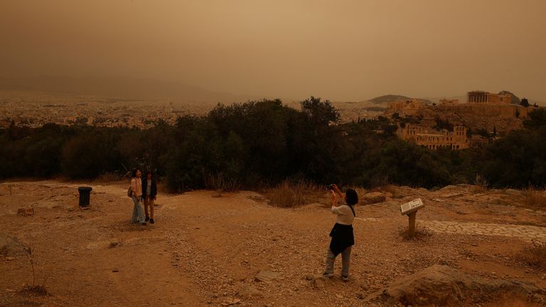 Tourists visit the Filipappou hill with the views of the Acropolis, as African dust from the desert of Sahara covers the city of Athens, Greece