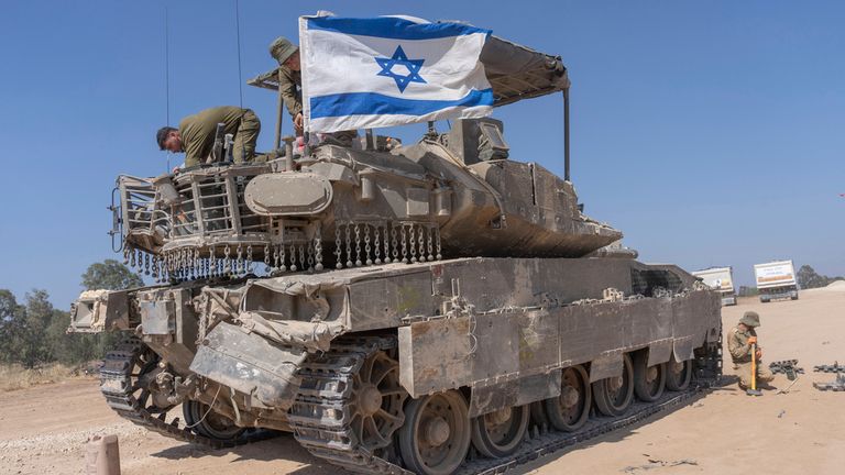 An Israeli soldier attaches an Israeli flag on top of an armoured personnel carriers (APC) near Israel's border with Gaza, in southern Israel, Monday, April 15, 2024. (AP Photo/Ohad Zwigenberg)