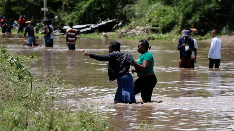 Residents wade through flood waters after Athi River burst its banks and marooned their homes. Pic: Reuters
