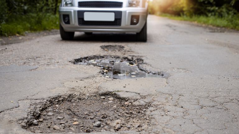 Road in terrible condition. Photo of a road with many potholes, chuckholes and driver driving the car very slow in order not to damage his vehicle