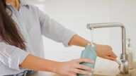 Close up of Woman fills up reusable water bottle in the kitchen