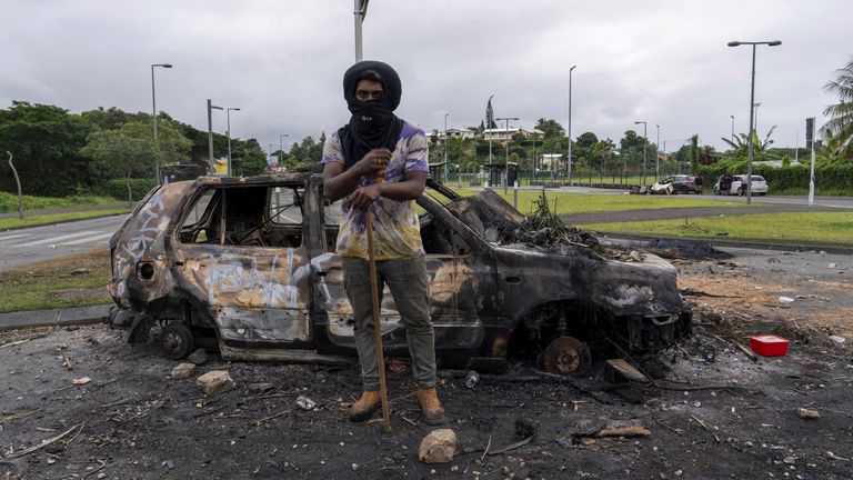 A man stands in front a burnt car after unrest in Noumea, New Caledonia, Wednesday May 15, 2024. France has imposed a state of emergency in the French Pacific territory of New Caledonia. The measures imposed on Wednesday for at least 12 days boost security forces&#39; powers to quell deadly unrest that has left four people dead, erupting after protests over voting reforms. (AP Photo/Nicolas Job)