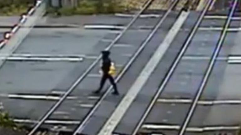 Man climbs barrier and crosses railway tracks as train approaches