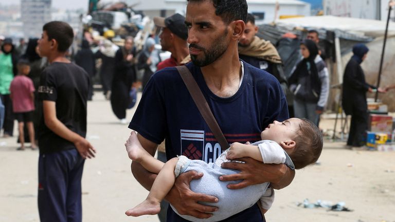 A man carries a child, as Palestinians flee Rafah due to Israeli strikes. Pic: Reuters