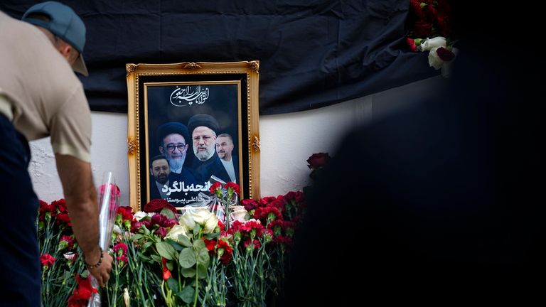 A man lays flowers near a photo of Iranian President Ebrahim Raisi and his colleagues at a makeshift memorial. Pic: AP