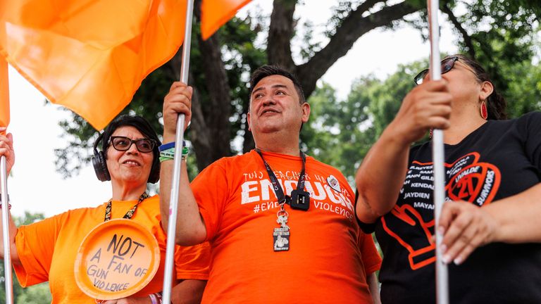 Robb Elementary shooting survivors Amy Franco, left, Arnulfo "Arnie" Reyes, center, stand with other survivors and community members at the town square on Friday morning, May 24, 2024, in Uvalde, Texas. The former Robb Elementary School educators waved orange flags signifying gun violence awareness to commemorate the 21 victims of the shooting ... 19 fourth-graders and two teachers ... who died two years ago Friday. (Sam Owens/The San Antonio Express-News via AP)