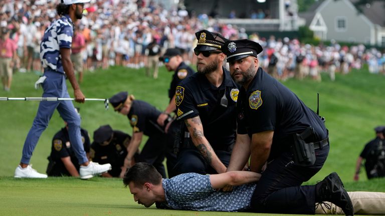 Protesters are taken into custody after they ran onto the course as Akshay Bhatia, left, walks away on the 18th hole during the final round of the Travelers Championship golf tournament at TPC River Highlands, Sunday, June 23, 2024, in Cromwell, Conn. (AP Photo/Seth Wenig)