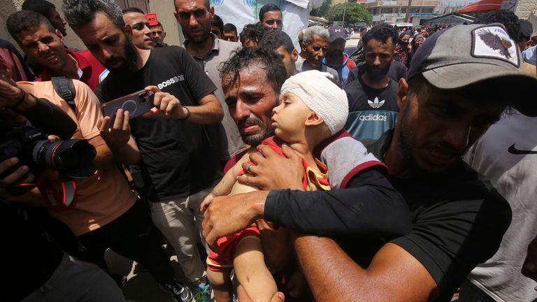 A Palestinian man carries a small child to receive medical treatment after Israeli attacks on the Nuseirat refugee camp