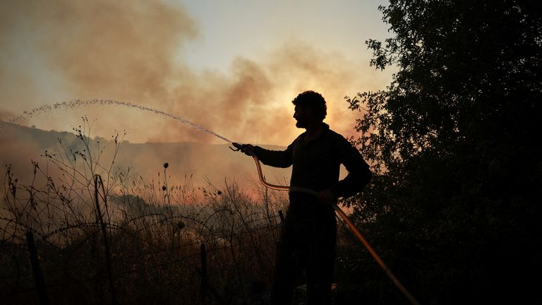 A man uses a hose to put out fires near Kiryat Shmona after rocket attacks from Lebanon. Pic: Reuters