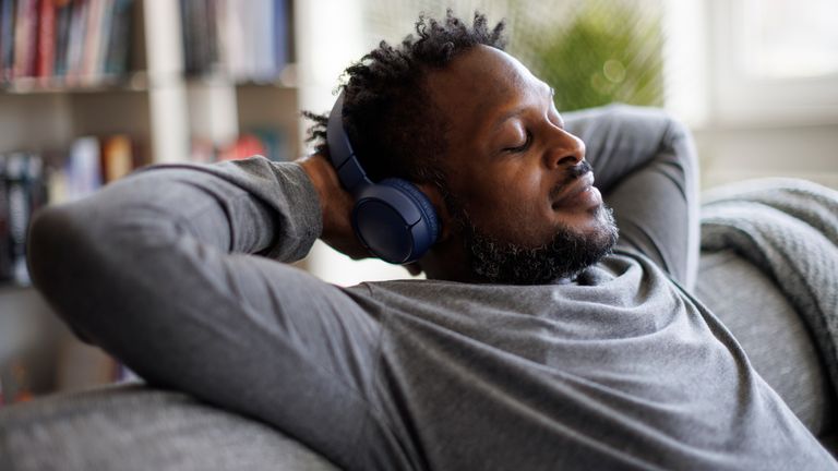 Young man enjoying music over headphones while relaxing on the sofa at home. Pic: iStock