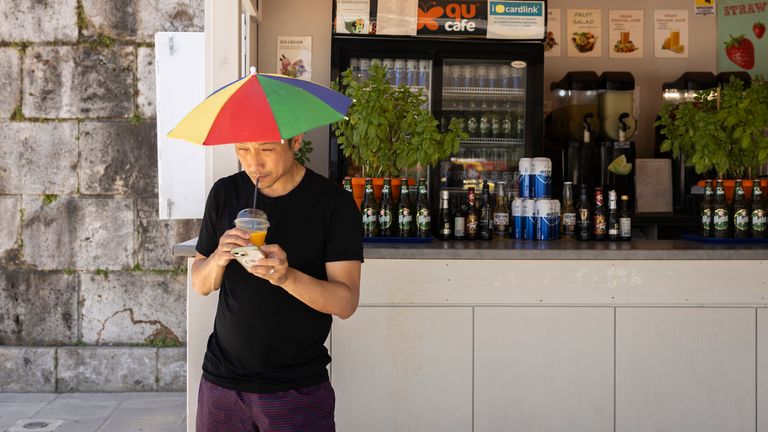 18 June 2024, Greece, Athen: A man wears a colorful umbrella on his head to protect himself from the sun and refreshes himself with a drink while visiting the Panathinaiko Stadium. Greece has been hit by extreme heat particularly early this year: According to meteorologists, it has never been this hot since records began in early June. Temperatures reached up to 40 degrees at times - and even higher in the blazing midday sun. Photo by: Socrates Baltagiannis/picture-alliance/dpa/AP Images


