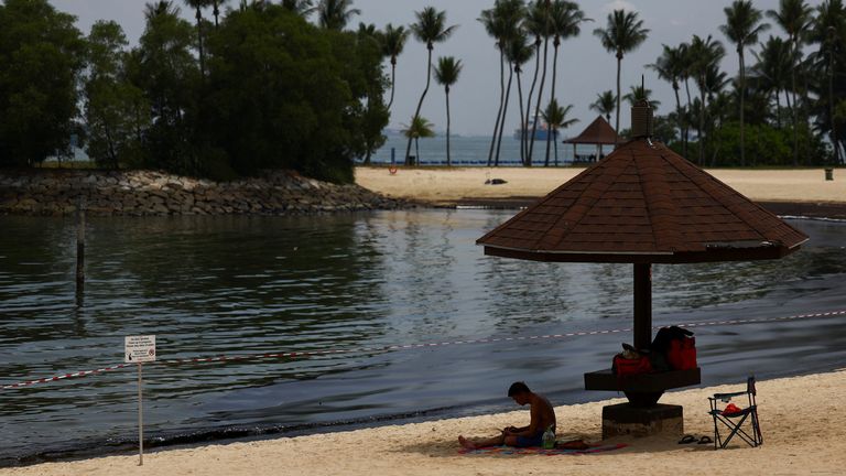 A man sits near signage and a cordon tape put up following an oil slick at Tanjong Beach in Sentosa, Singapore.
Pic: Reuters