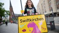 Schoolgirl Aleshanee Westhoff shows a "Swiftkirchen" town sign in honor of musician Taylor Swift in Gelsenkirchen, Germany, Tuesday, July 2, 2024. The Swifties are about to take over the German city of Gelsenkirchen, where American superstar Taylor Swift is set to give three concerts of her Eras Tour later this month. In honor of the singer, the city renamed itself “Swiftkirchen" — at least temporarily to welcome the tens of thousands of fans who are expected to come for the Eras Tour shows on J