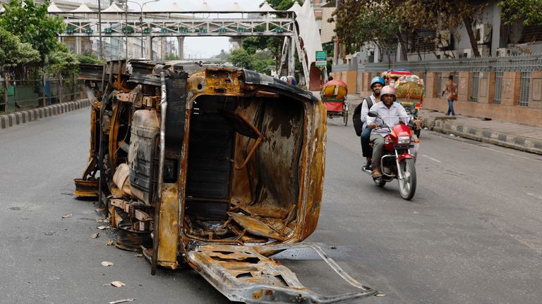 Men ride on a motorbike past a damaged vehicle that was set on fire.
Pic: Reuters