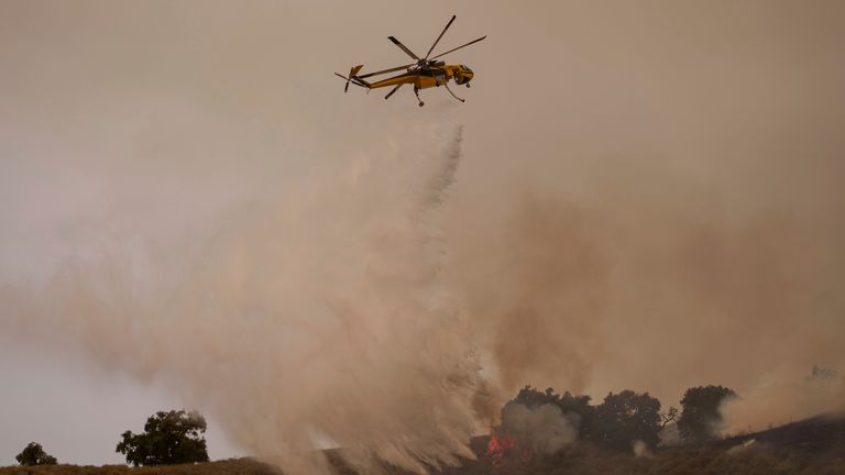 A helicopter drops water on flames from the advancing Lake Fire in Los Olivos, California, Saturday, July 6, 2024. (AP Photo/Eric Thayer)