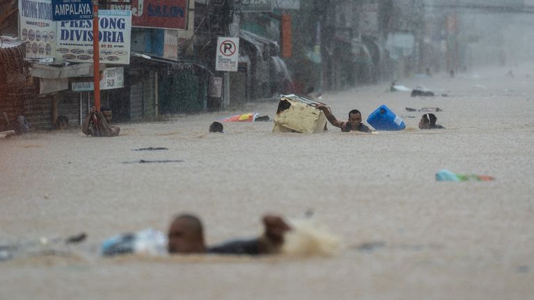 People wade through a flooded road on the outskirts of Manila, Philippines. Pic: Reuters