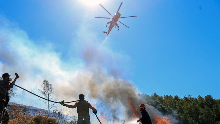 A helicopter flies over a firefighter and volunteers trying to extinguish a wildfire burning in Keratea.
Pic: Reuters